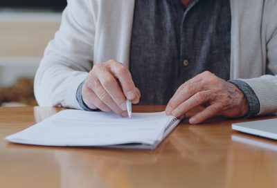 Hands of senior retirement woman writing a finance savings budget plan on paper or legal trust fund for after her funeral. Elderly person apply for pension or government financial support and help Hands of senior retirement woman writing a finance savings budget plan on paper or legal trust fund for after her funeral. Elderly person apply for pension or government financial support and help